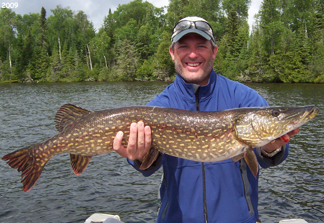 This is a photo of a man in a blue jacket holding up a 20 pound Northern Pike
