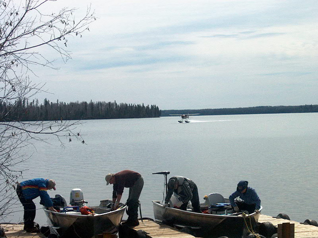 This is a photo of men getting their boats ready while the floatplane lands on the lake behind them