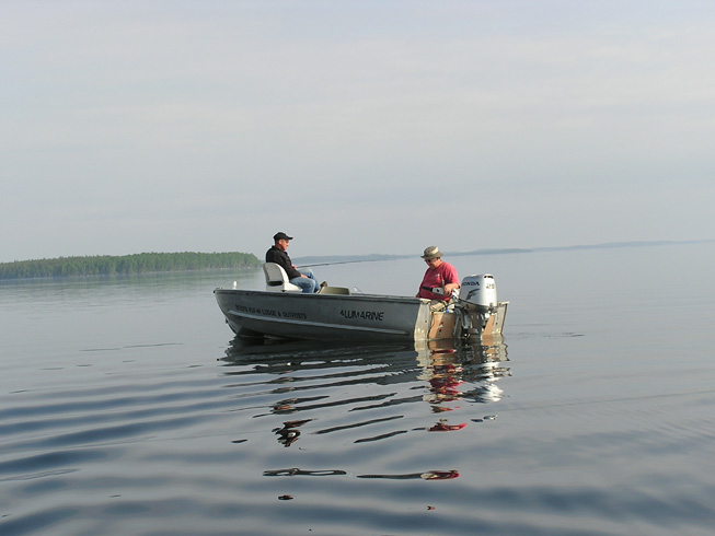 This is a photo of two men fishing in a boat out on the open water for Lake Trout